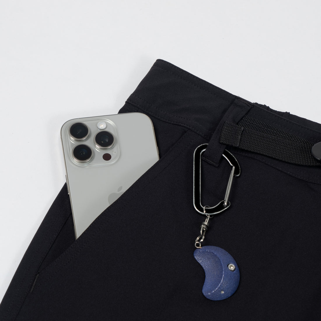Phone case with carabiner and moon charm attached to black pants on a white background
